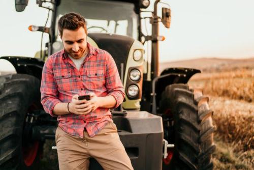Portrait of smiling farmer using smartphone 和 tractor at harvesting.